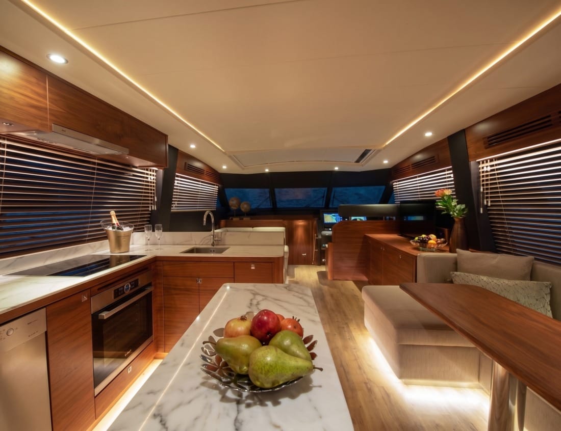 Warmly lit interior of a Phantom 65 Coupé yacht (P-series) with a wood-finished galley, marble countertops and dining area.