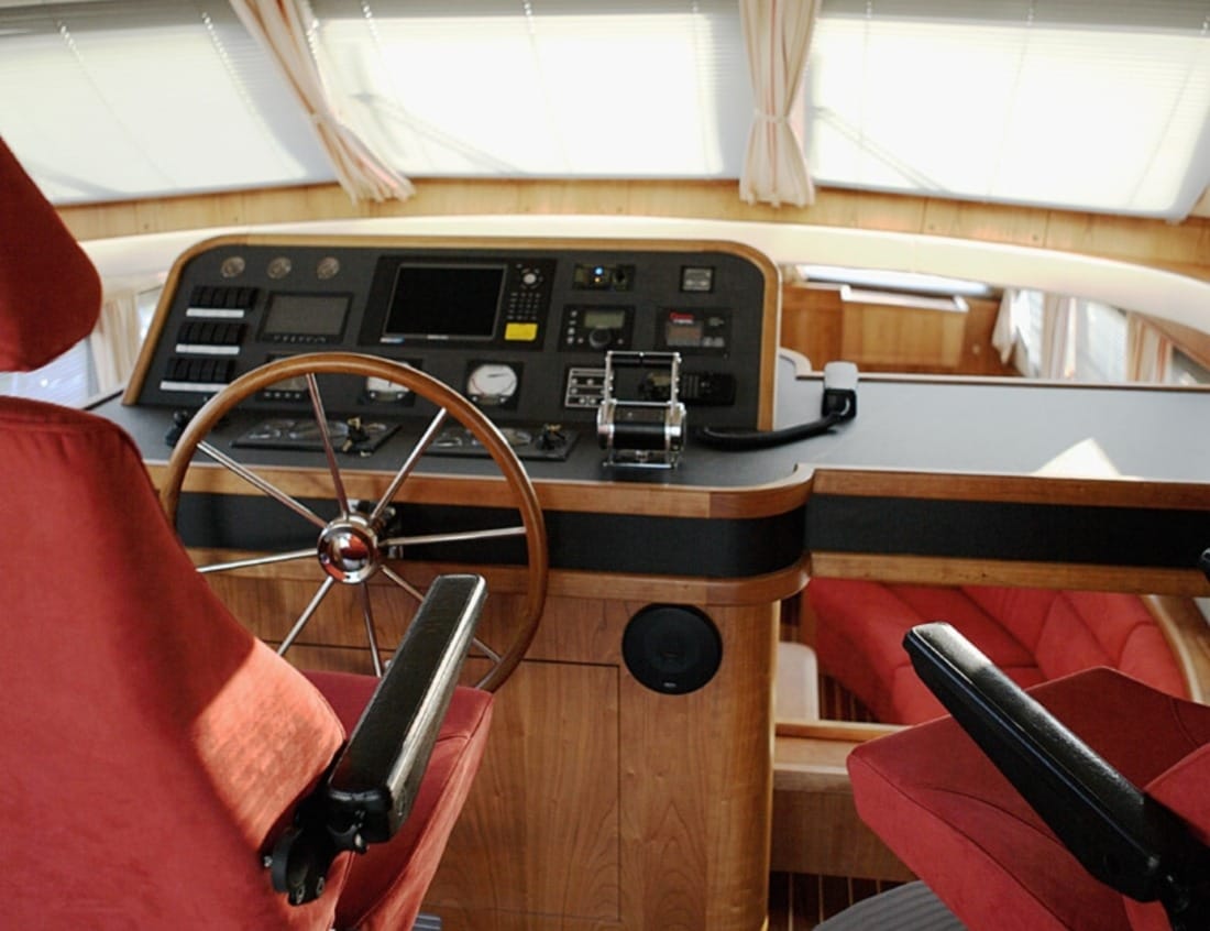Helm station of a Dynamic Deluxe 1800 - Dynamic Series with steering wheel, navigation controls and red captain’s chairs.